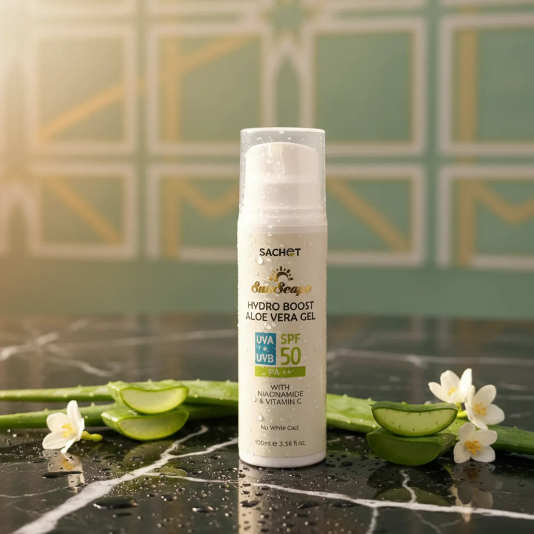 Sachet Hydro Boost Aloe Vera Gel SPF 50 on a dark surface with aloe vera leaves and flowers, against a green tiled wall.